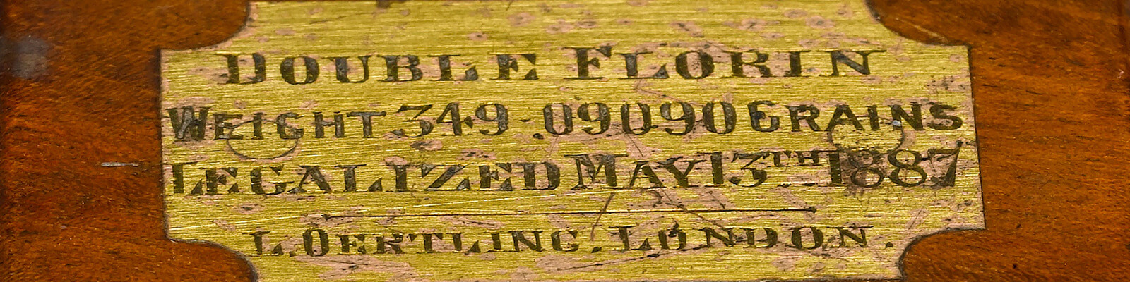 A close up of the gold label from the top of a wooden box that contains weights for the double florin coin