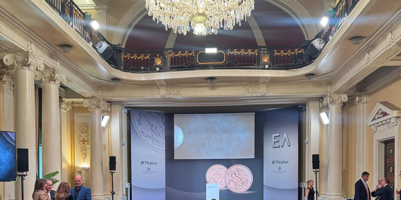An extravagant ball room set up with chairs and a projection for a talk with a large crystal chandelier above