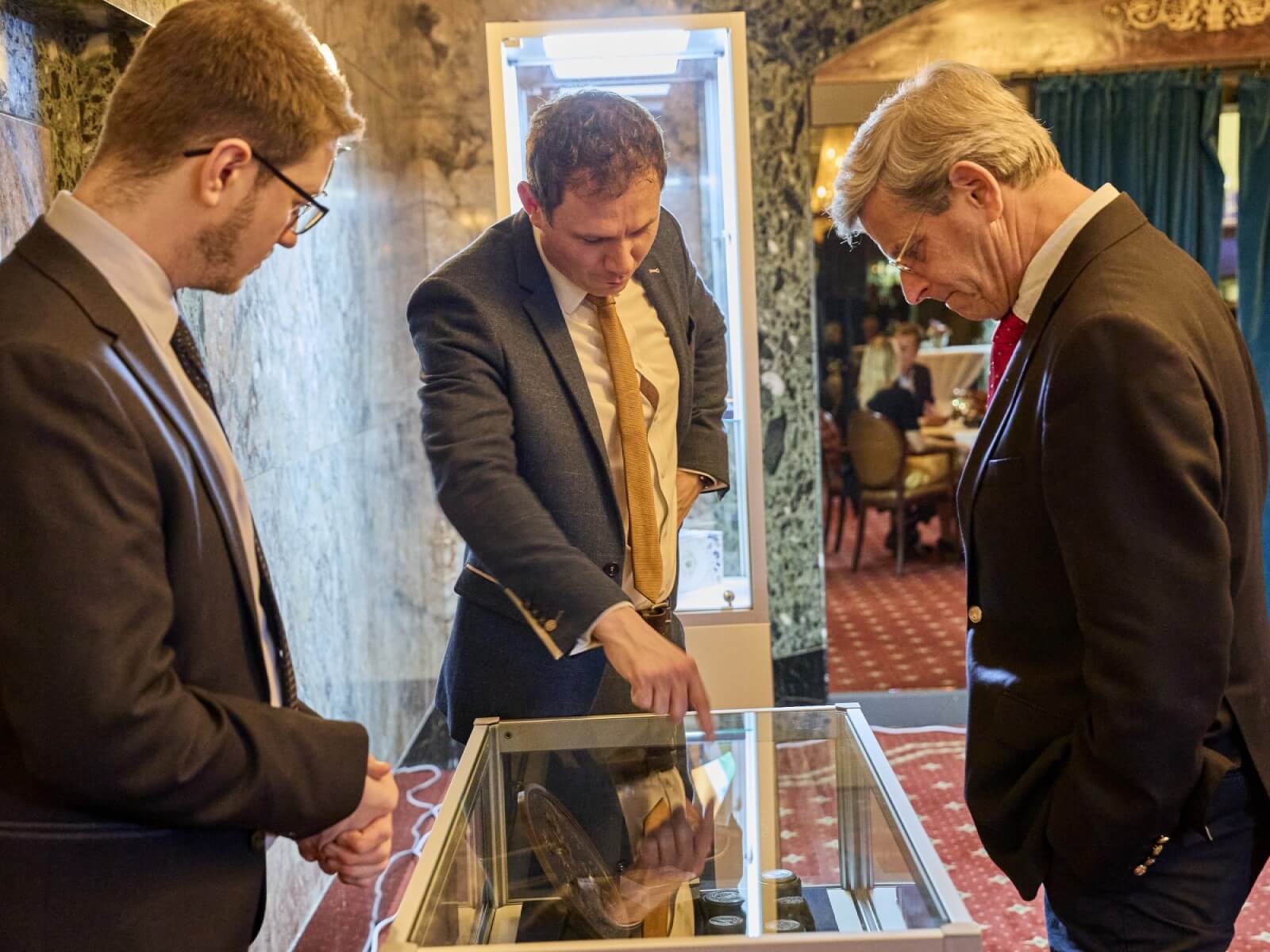 Three men stand around a display case