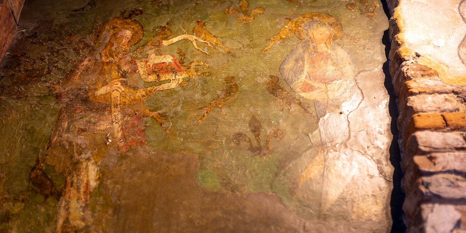 An old wall painting featuring medieval characters on a green background. The painting is worn and has lots of holes