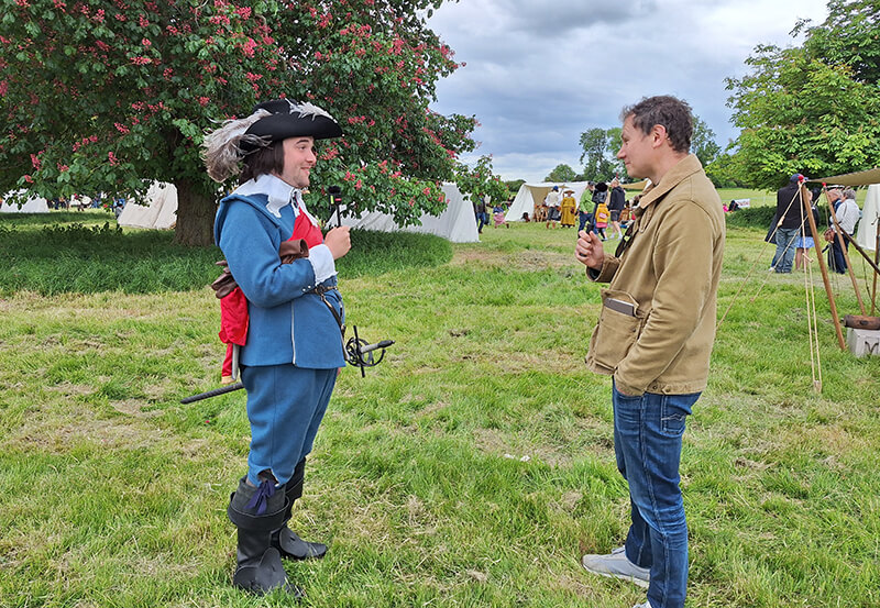 Chris Barker standing in a field interviewing a member of the Sealed Knot society in character as a Royalist Officer
