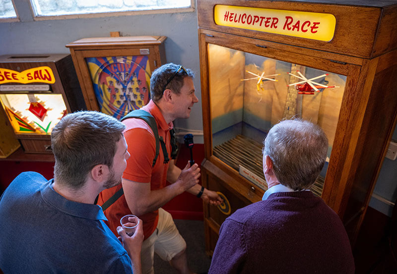 David Mason, Chris Barker and Peter Williamson playing on an old penny arcade machine called 'Helicopter Race'